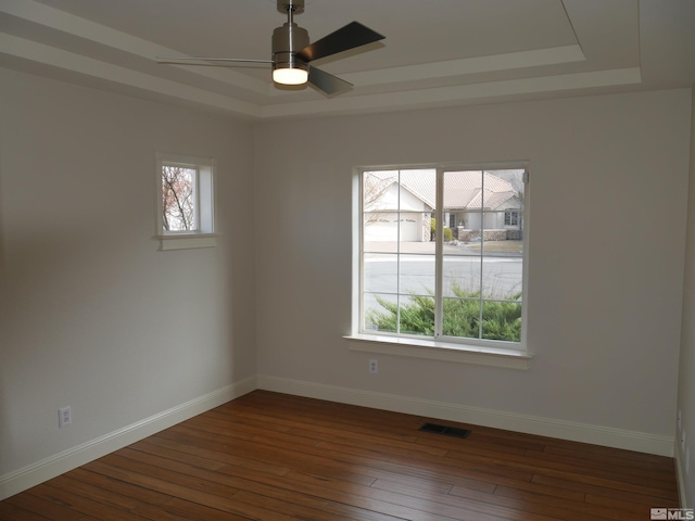 empty room featuring dark wood-style flooring, a raised ceiling, visible vents, a ceiling fan, and baseboards