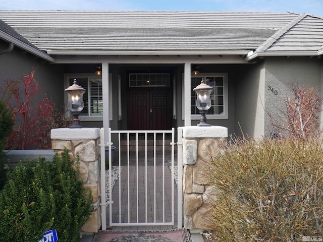 property entrance with a gate, a tile roof, and stucco siding