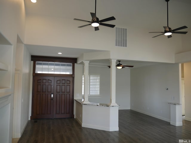 entryway with a towering ceiling, ornate columns, visible vents, and dark wood finished floors