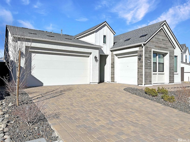 view of front of property featuring decorative driveway, roof with shingles, board and batten siding, a garage, and stone siding