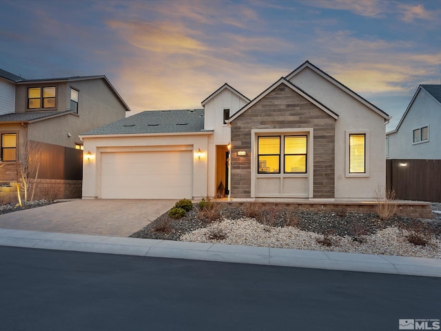 view of front of house with a garage, a shingled roof, stone siding, fence, and decorative driveway