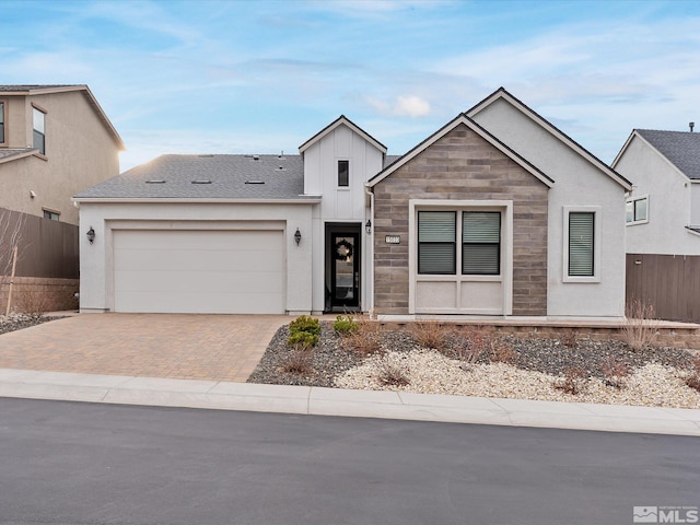 view of front of home featuring a garage, a shingled roof, stone siding, decorative driveway, and board and batten siding