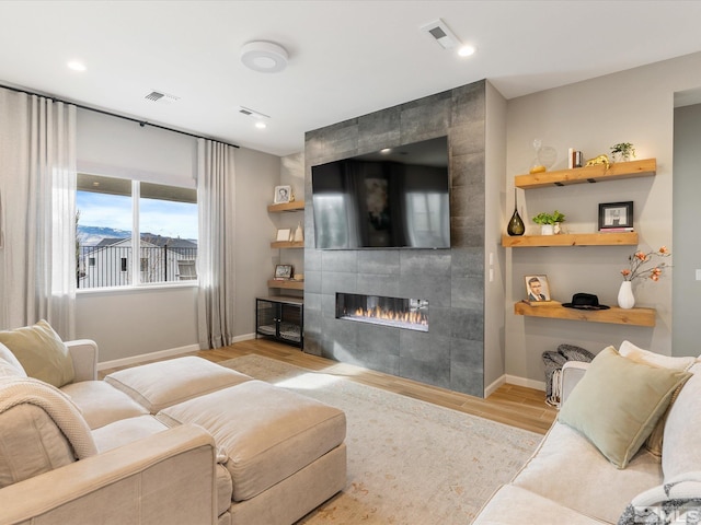 living area with a tiled fireplace, wood finished floors, visible vents, and baseboards