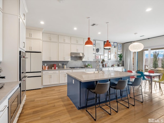 kitchen featuring a breakfast bar, stainless steel appliances, light countertops, visible vents, and under cabinet range hood