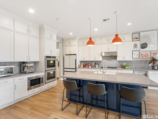 kitchen with appliances with stainless steel finishes, a breakfast bar, visible vents, and under cabinet range hood