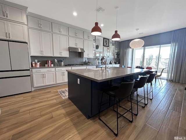 kitchen with under cabinet range hood, a sink, visible vents, white refrigerator, and stovetop