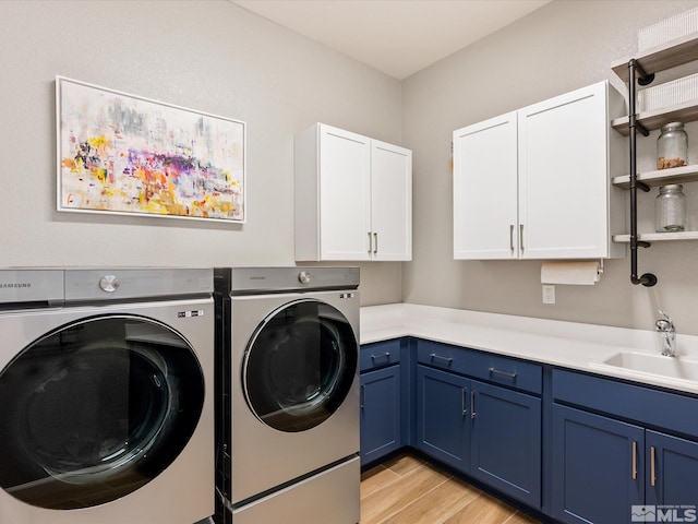 laundry area with cabinet space, separate washer and dryer, a sink, and light wood finished floors