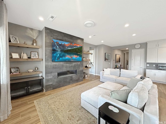 living room featuring light wood-type flooring, recessed lighting, visible vents, and a tile fireplace