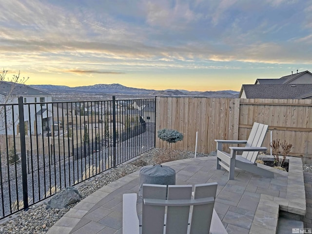 patio terrace at dusk featuring a fenced backyard and a mountain view