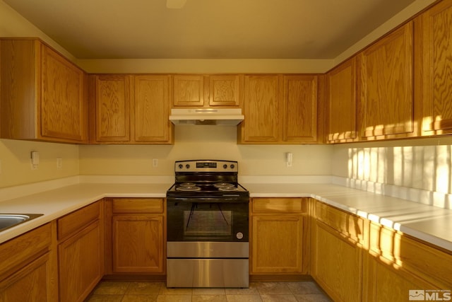 kitchen with brown cabinetry, electric range, light countertops, and under cabinet range hood