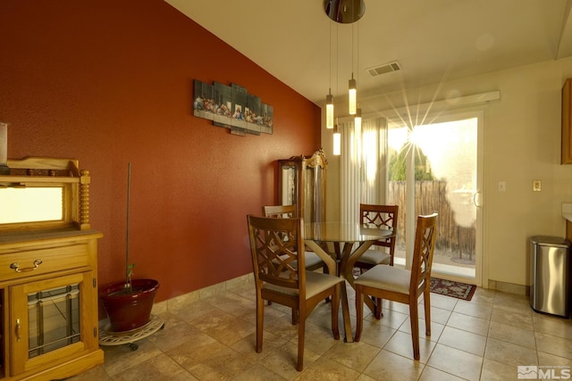 dining space with visible vents, vaulted ceiling, a glass covered fireplace, and light tile patterned flooring