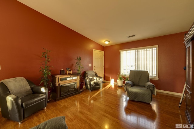 living area with baseboards, visible vents, wood finished floors, vaulted ceiling, and a fireplace