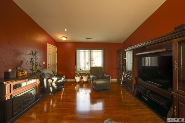 living room featuring lofted ceiling, wood finished floors, visible vents, and baseboards