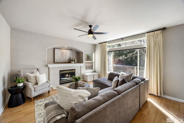 living area featuring a ceiling fan, baseboards, light wood-style flooring, and a tiled fireplace