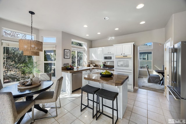 kitchen featuring arched walkways, recessed lighting, stainless steel appliances, a center island, and dark countertops