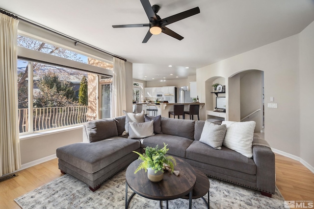 living area with light wood-type flooring, ceiling fan, arched walkways, and baseboards