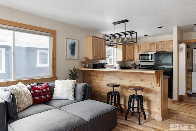 kitchen featuring light wood-style flooring, stainless steel microwave, open floor plan, a breakfast bar area, and a peninsula