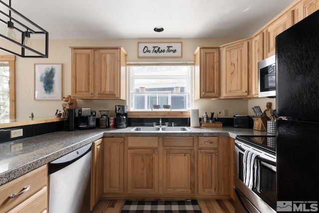 kitchen featuring dark countertops, light wood-style floors, stainless steel appliances, and a sink