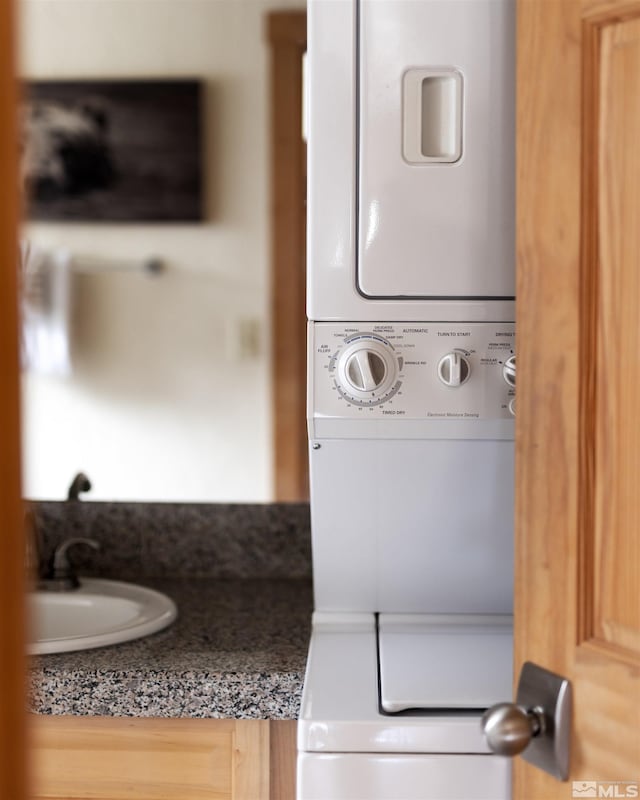 washroom with stacked washer / drying machine, laundry area, and a sink