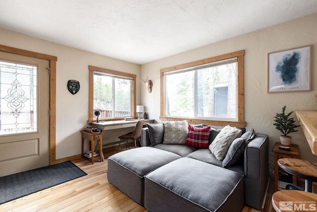 living area featuring a textured wall, light wood-style flooring, and baseboards