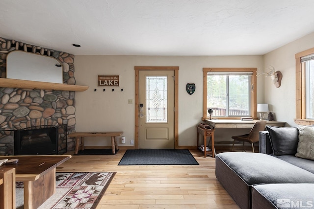 living room with a stone fireplace, light wood-type flooring, and baseboards