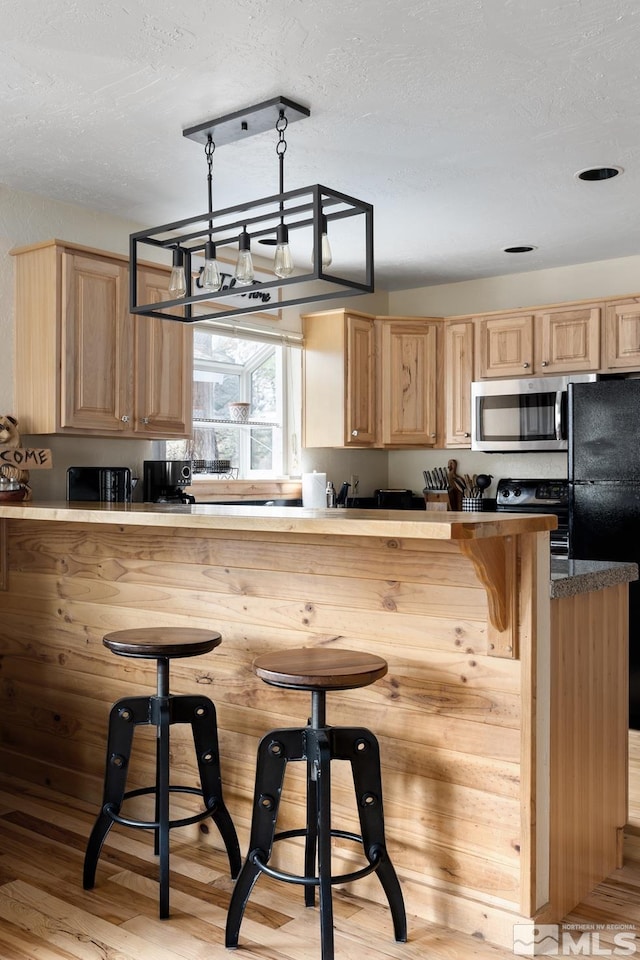 kitchen with a breakfast bar, stainless steel microwave, and light brown cabinets