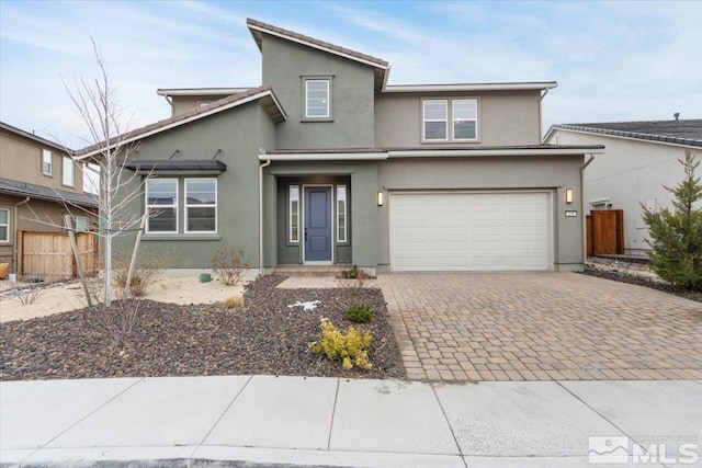 traditional-style home with decorative driveway, an attached garage, fence, and stucco siding