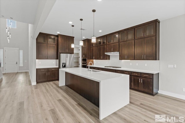 kitchen with stainless steel appliances, a sink, light countertops, light wood-type flooring, and backsplash