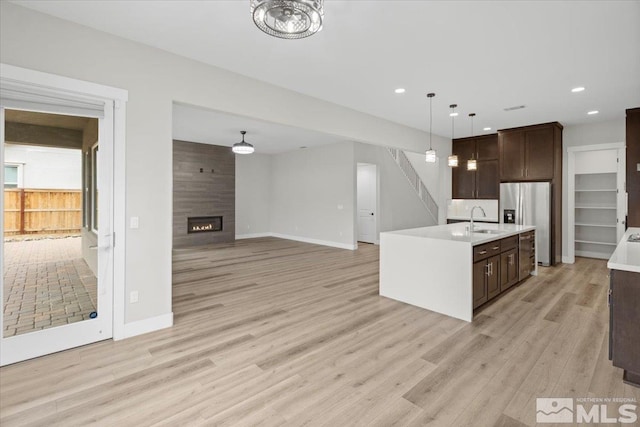 kitchen with dark brown cabinetry, a sink, light countertops, light wood finished floors, and stainless steel fridge