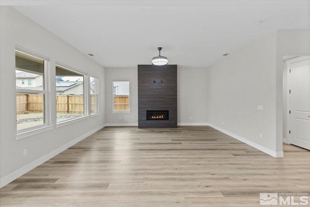 unfurnished living room with light wood-style floors, a large fireplace, and baseboards