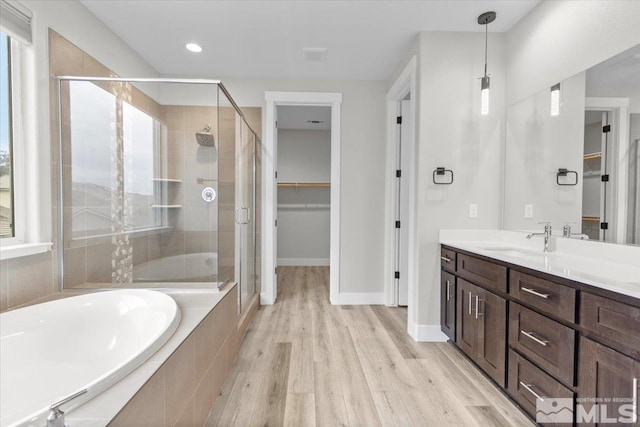 full bathroom featuring a garden tub, wood finished floors, vanity, a stall shower, and a walk in closet