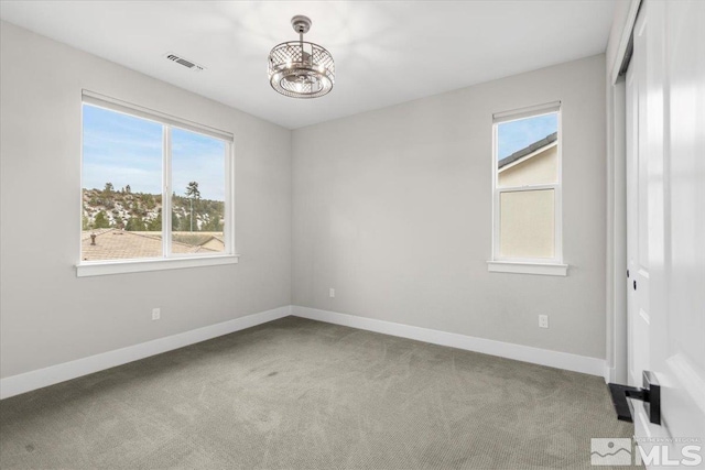 empty room with carpet floors, visible vents, baseboards, and a chandelier