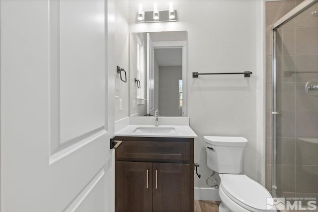 bathroom with vanity, a tile shower, toilet, and baseboards