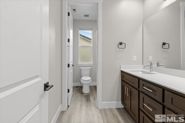 bathroom with toilet, wood finished floors, visible vents, vanity, and baseboards