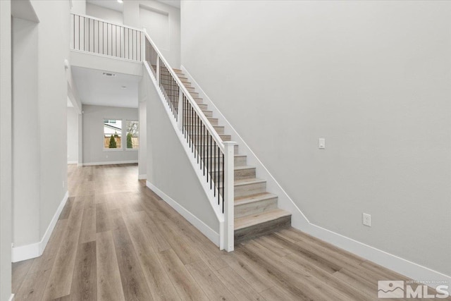 stairs featuring a towering ceiling, baseboards, and wood finished floors