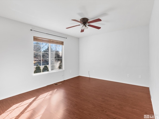 spare room with a ceiling fan, visible vents, baseboards, and wood finished floors