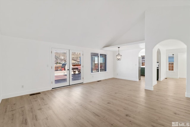 unfurnished living room with baseboards, arched walkways, a chandelier, light wood-type flooring, and high vaulted ceiling