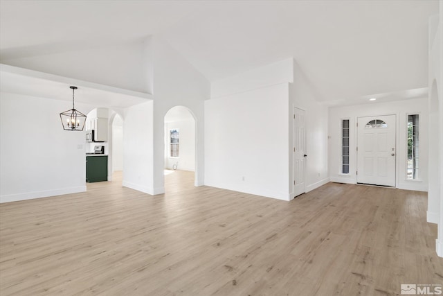 unfurnished living room featuring arched walkways, high vaulted ceiling, a notable chandelier, baseboards, and light wood-style floors