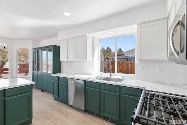 kitchen featuring stainless steel appliances, light wood-style floors, white cabinetry, a sink, and green cabinetry