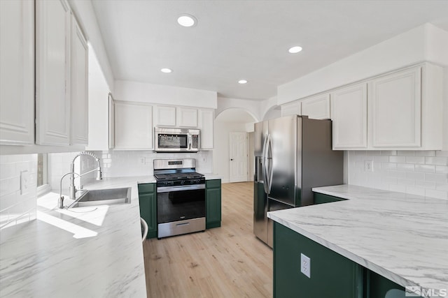 kitchen with a sink, white cabinetry, appliances with stainless steel finishes, light stone countertops, and light wood finished floors