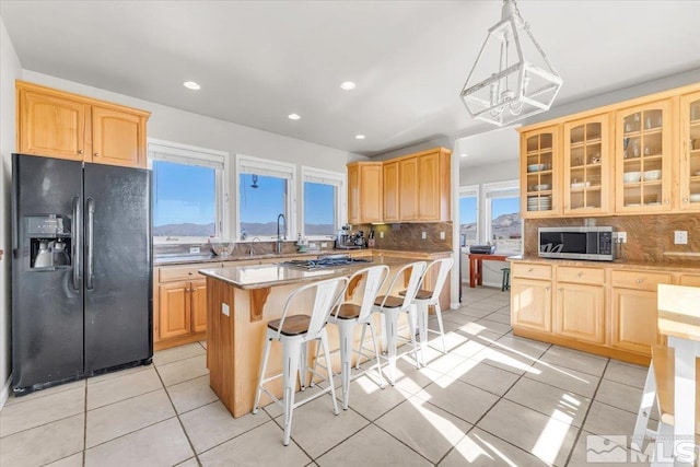 kitchen featuring a breakfast bar area, light tile patterned flooring, black fridge with ice dispenser, stainless steel microwave, and glass insert cabinets