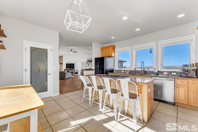 kitchen with a kitchen island, a breakfast bar, stainless steel appliances, light brown cabinetry, and a sink