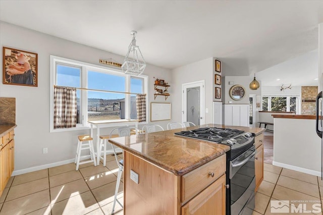 kitchen with light tile patterned floors, a kitchen breakfast bar, a center island, stainless steel gas range, and light brown cabinetry