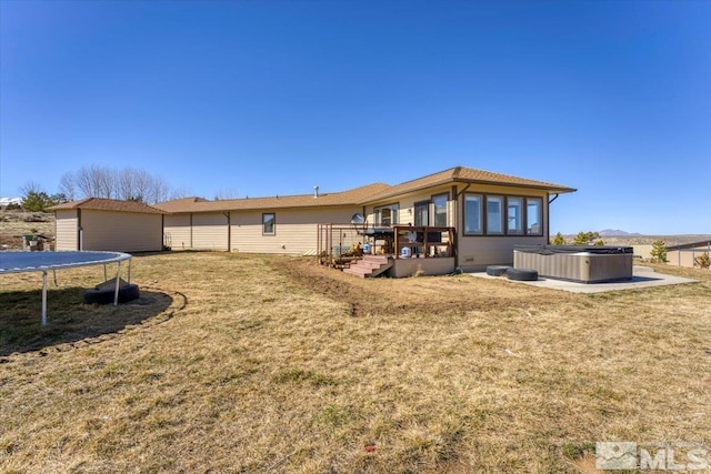 rear view of property featuring a hot tub, a wooden deck, an outbuilding, a trampoline, and a yard