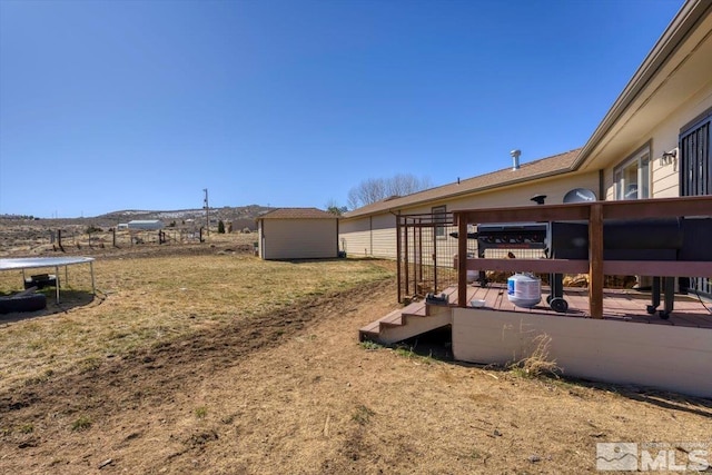 view of yard featuring an outbuilding, a deck, a trampoline, and a storage unit