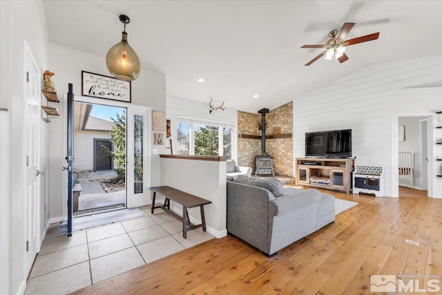 living area featuring a ceiling fan, a wood stove, vaulted ceiling, and light wood finished floors