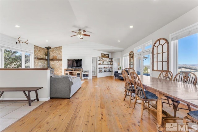 dining space featuring light wood-type flooring, lofted ceiling, a wood stove, and plenty of natural light