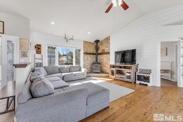 living room featuring a wood stove, vaulted ceiling, light wood finished floors, and ceiling fan