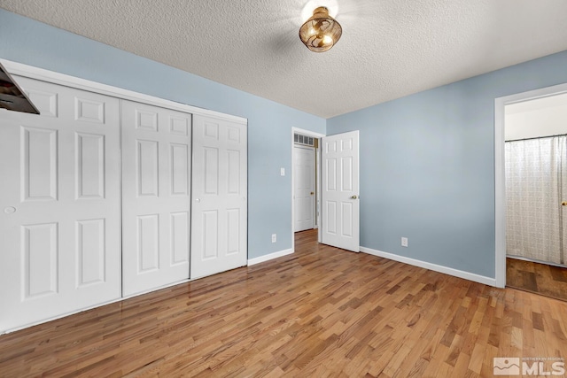 unfurnished bedroom with a textured ceiling, light wood finished floors, a closet, and baseboards