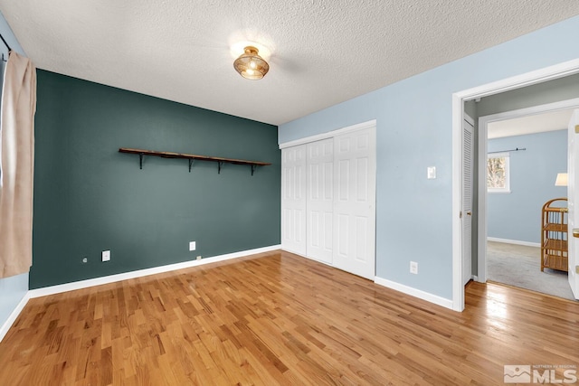 unfurnished bedroom with a closet, light wood-style flooring, baseboards, and a textured ceiling